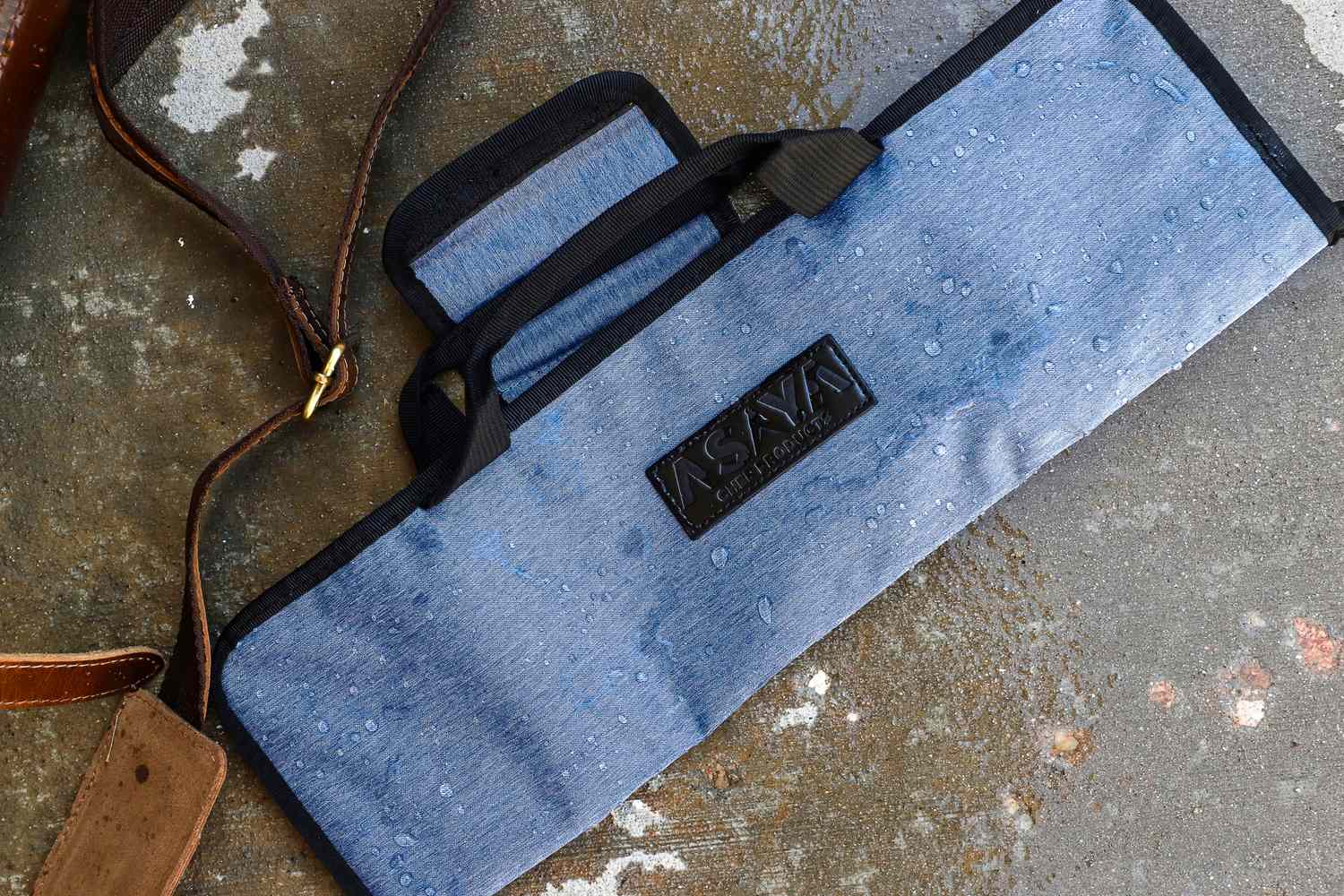 A waterresistantAsaya Chef Knife Roll Bag with handles and a leather strap on a textured surface