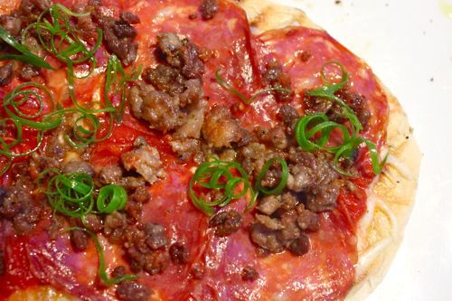 A pizza topped with meat, sauce, cheese, and grilled scallions.