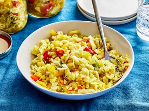 Bowl of Chow Chow with a spoon in it. The bowl is on a blue table cloth with other plates and sparkling water around it 