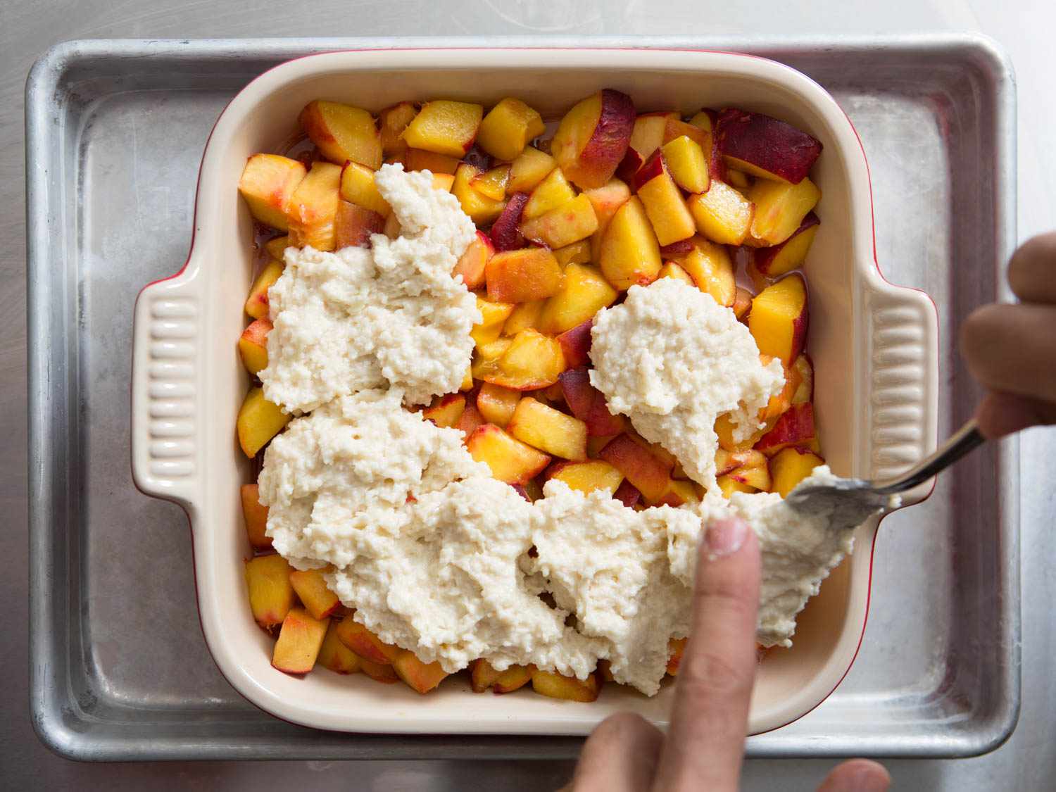 Adding biscuit topping on top of diced peach for peach cobbler. 