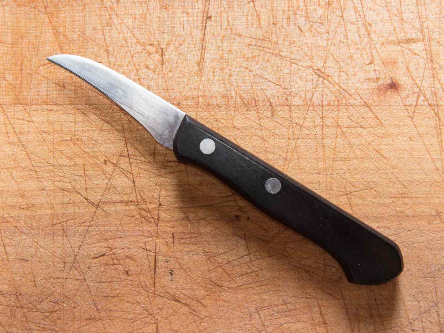 A tourné knife on a wooden cutting board.