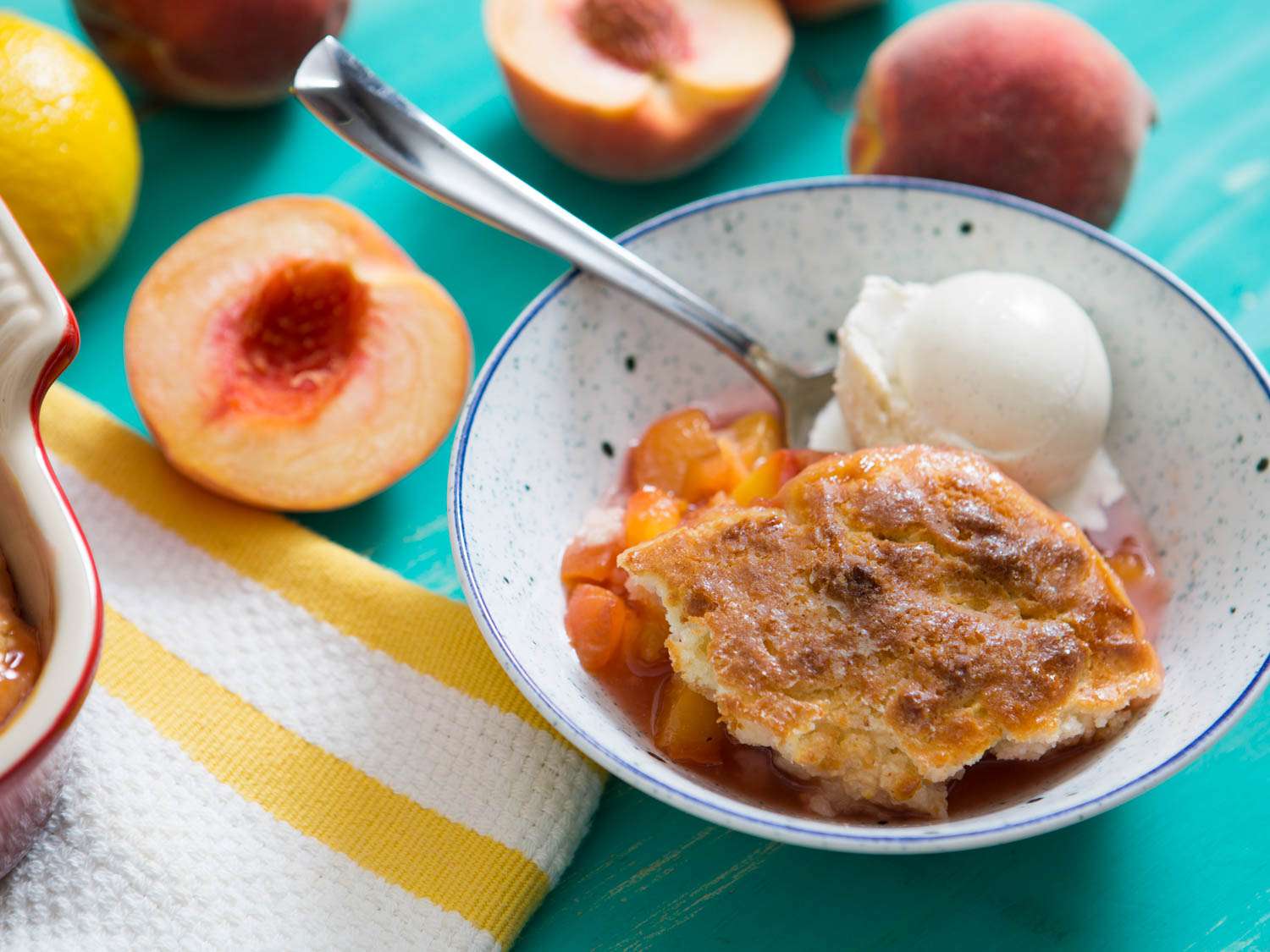 A bowl of peach cobbler with a scoop of ice cream next to split peaches.