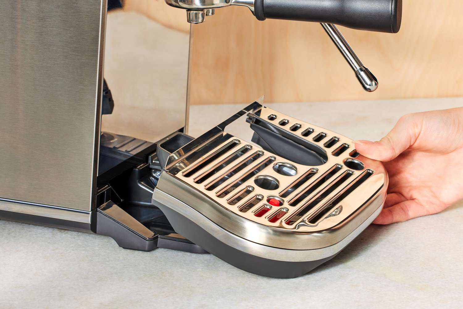 Person's hand adjusting tray of Breville Bambino Plus Espresso Machine on a cream counter