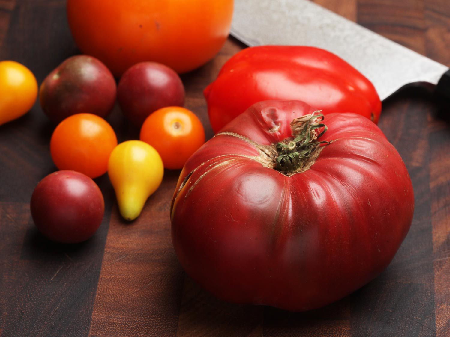 A variety of tomatoes in irregular shapes laying on a wooden work surface. 
