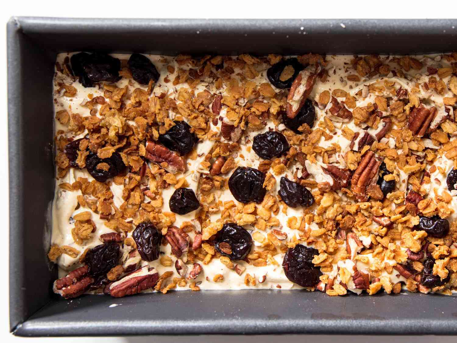 Loaf pan filled with oatmeal cookie ice cream, covered in dried fruit, nuts, and oat clusters.