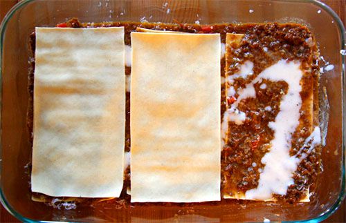 Overhead of layering meat sauce, noodles, besciamella for lasagna bolognese.