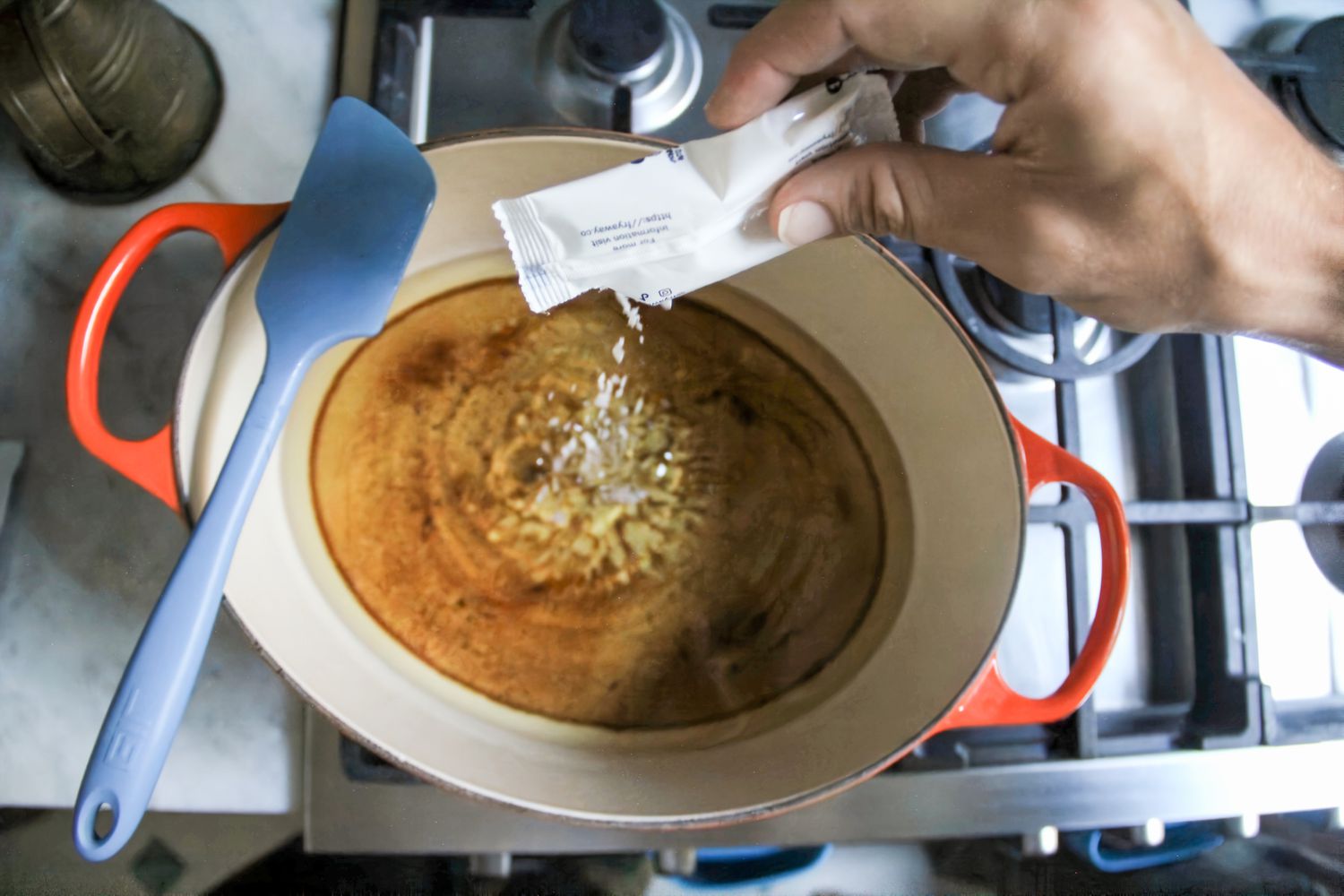 A hand pouring a packet of FryAway Pan Fry Cooking Oil Solidifier into a pan of oil