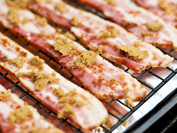 Brown sugar sprinkling on top of bacon slices on a wire rack. 