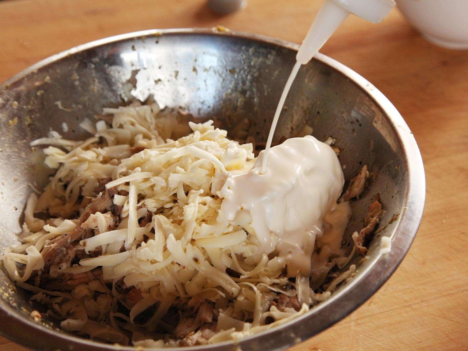 Picked and shredded chicken is combined in a bowl with shredded cheese and crema.
