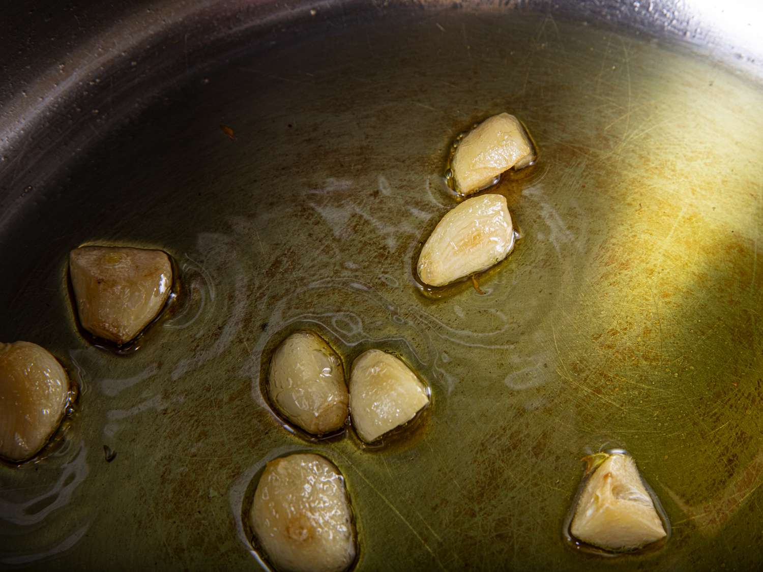 Whole or almost whole garlic cloves slowly cooking in oil in a pan