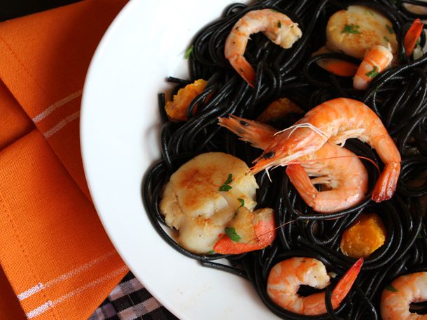 Close-up of a plate of the squid ink pasta. Head-on shrimp and large scallops stud the ebony strands of tonnarelli pasta.