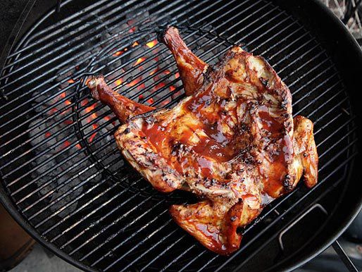 Butterflied chicken lying breast-side down on the grill grate. Its back has been liberally brushed with barbecue sauce.