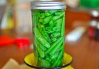 Closeup of a sealed glass jar of pickled sugar snap peas set on top of inverted yellow colander