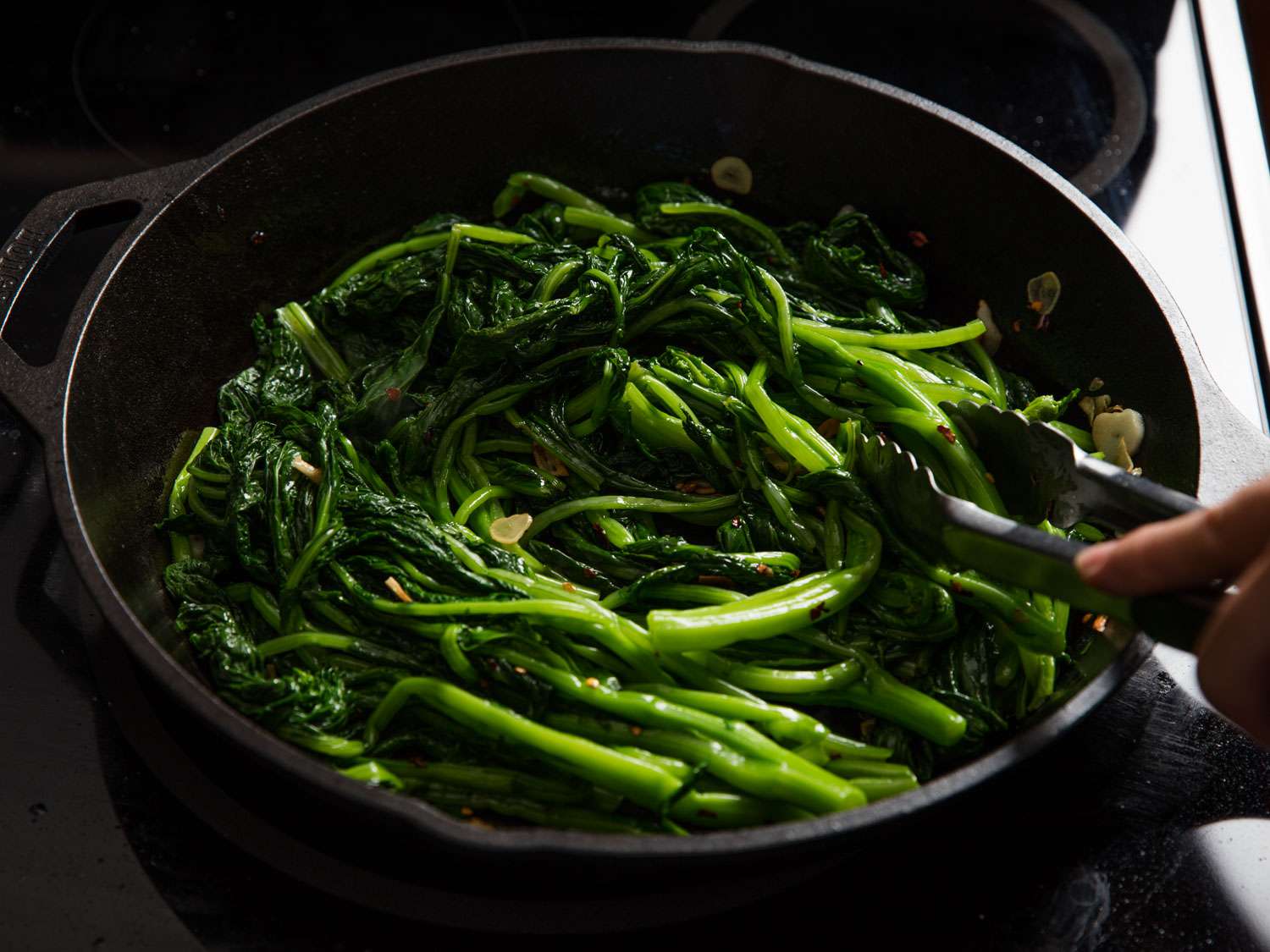 Sautéing broccoli rabe in a skillet, using tongs to move it around.