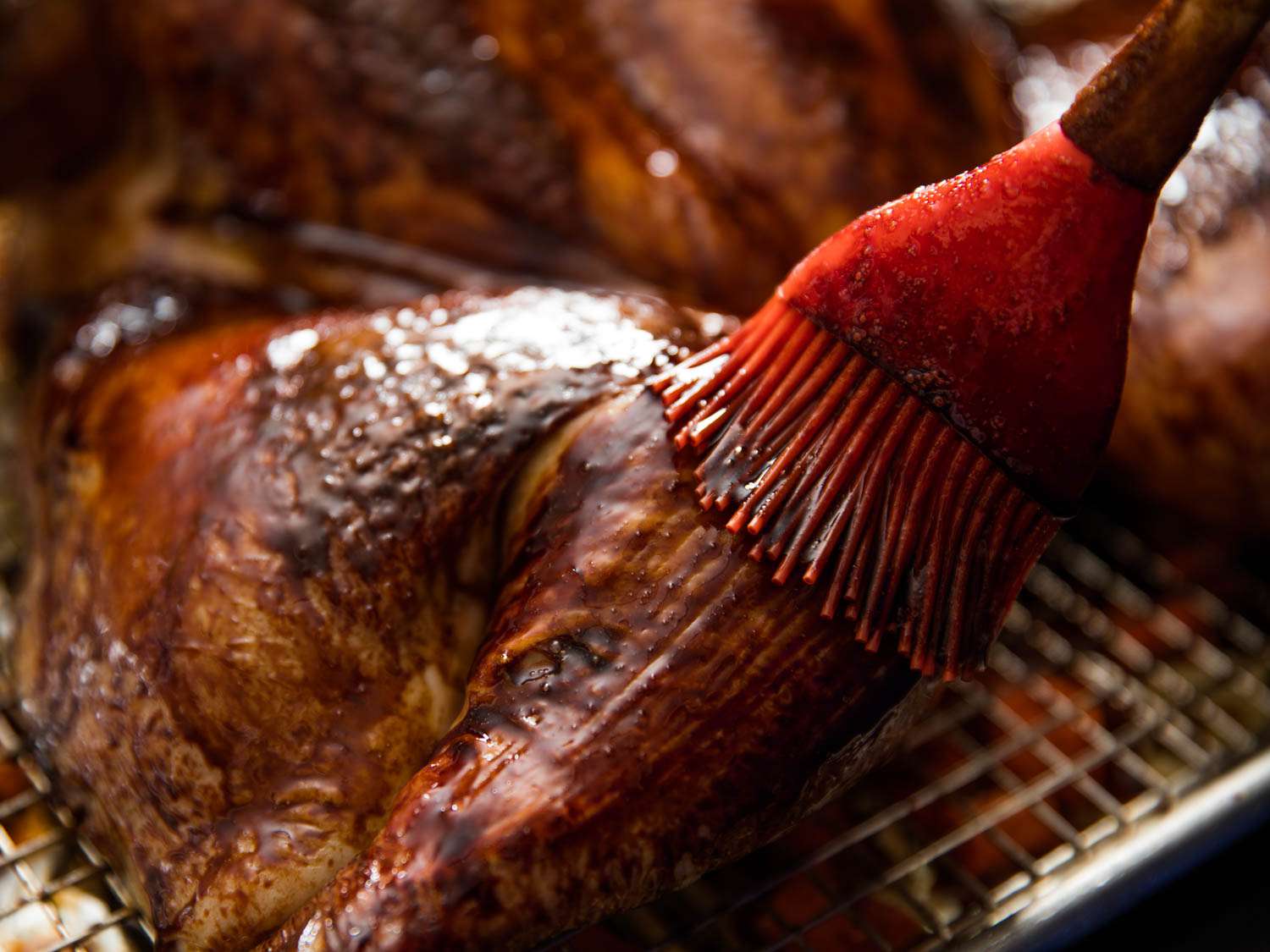 Closeup of the leg quarter of a turkey being brushed with a Chinese red sauce glaze.