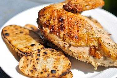 Closeup of a breast and attached wing of Cornell chicken, served with grilled potato slices.