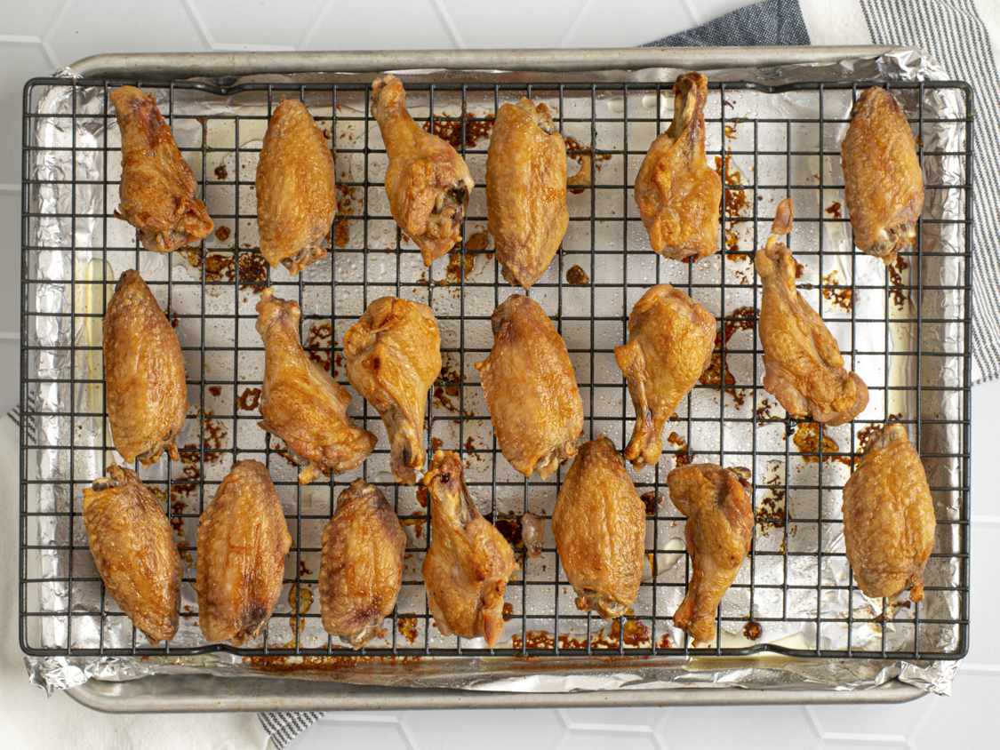 The roasted (oven-fried) chicken wings on a wire rack set inside of a foil-lined rimmed baking sheet.
