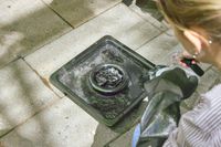 A person adds water to a burner on the Cuisinart COS-244 Vertical 36-inch Propane Smoker