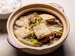 A clay pot filled with Frozen Simmered Tofu Soup with Pork, Cabbage, and Rice Noodles with rice alongside