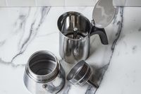 Parts of a stovetop espresso maker shown disassembled on a marble countertop