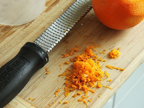 Orange zest next to an orange and a microplane grater on a cutting board. 