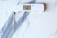 A white Thermapen ONE thermometer with its probe extended on a marble countertop.