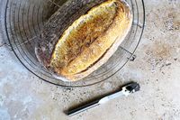 An overhead view of a bread loaf next to a stainless steel bread lame