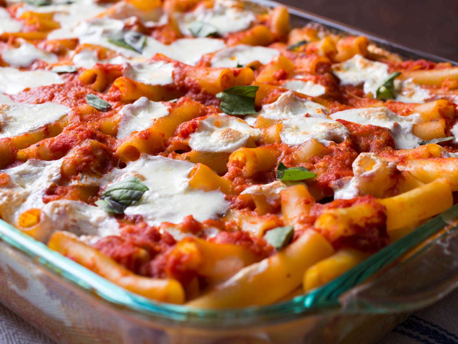Close-up of bake ziti with pools of melted cheese and torn basil.