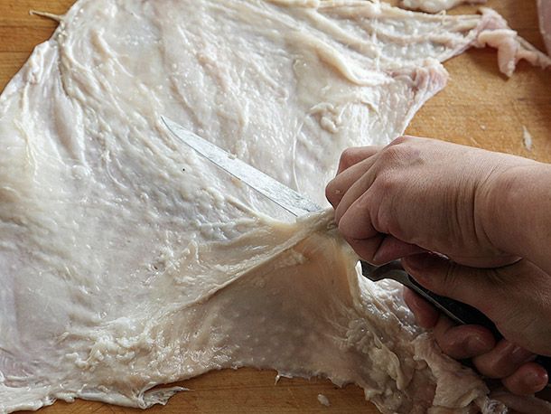 Trimming excess fat pockets from a whole piece of turkey breast skin.