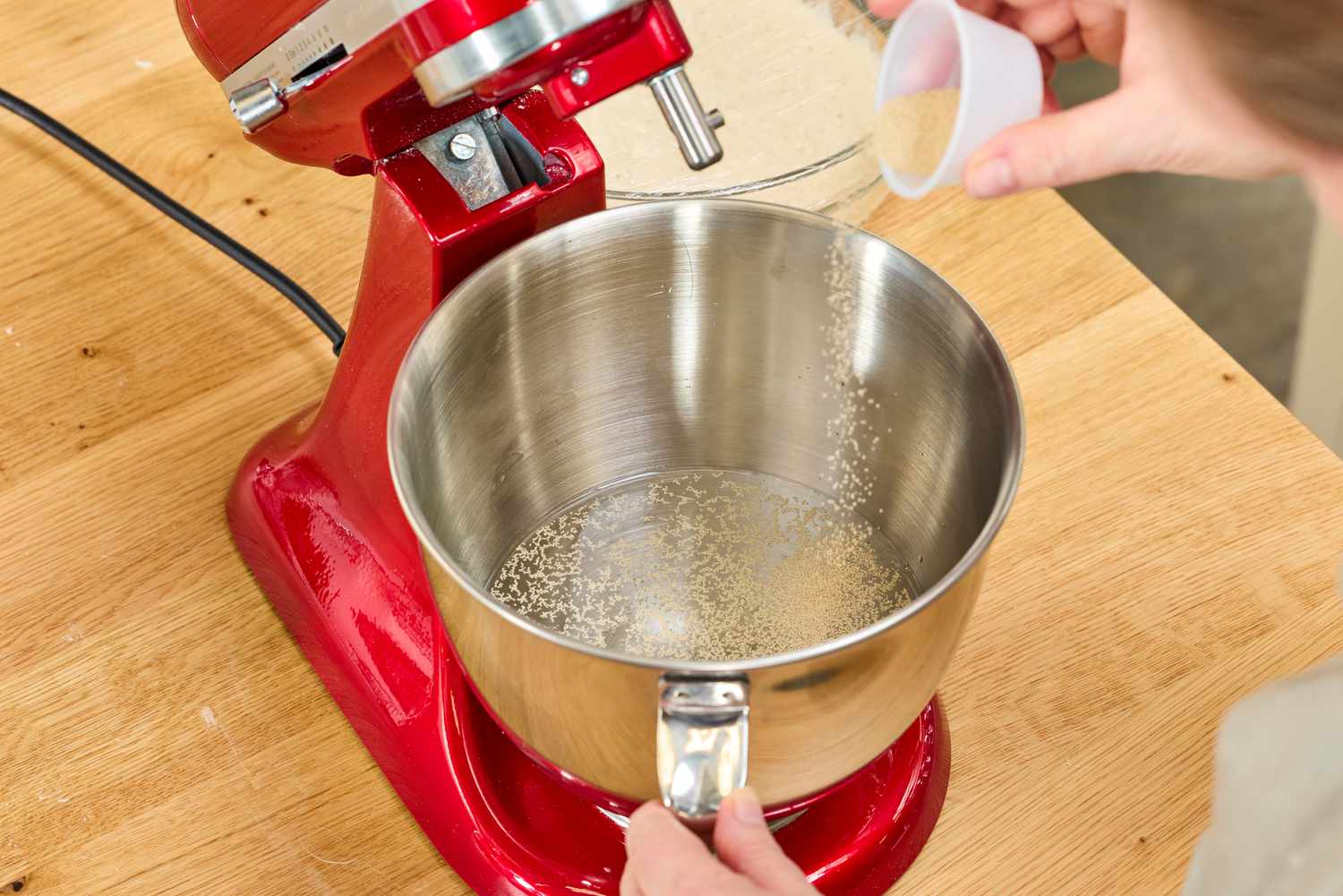 A person pours yeast into the KitchenAid Artisan Mini 3.5-Quart Tilt-Head Stand Mixer