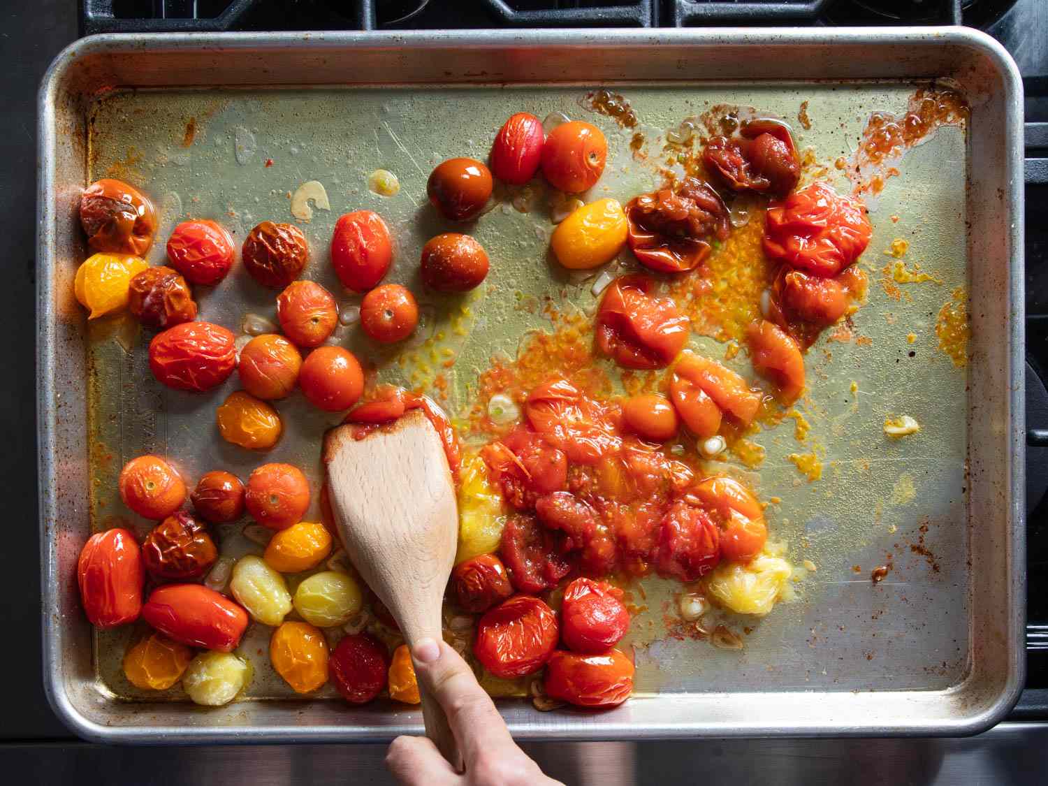 Mashing roasted tomatoes and garlic together on a sheet pan