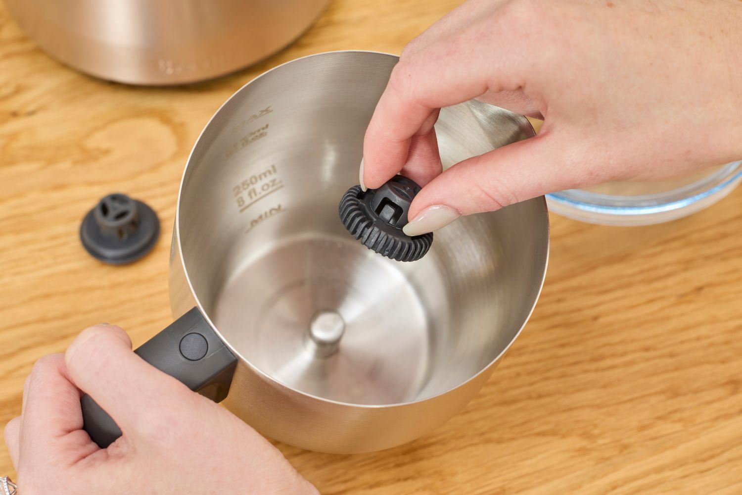 A person adding a whisk to the Breville milk frother's pitcher.