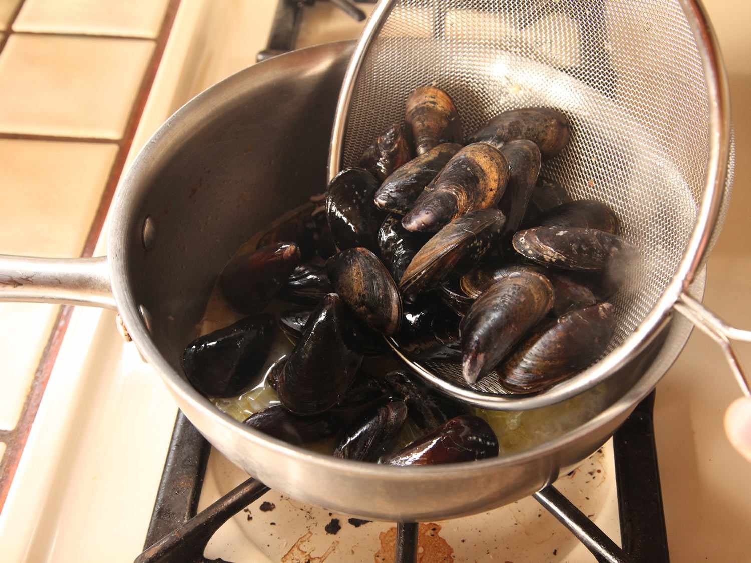 Mussels are added to the pan from the fine mesh strainer they were rinsed in.