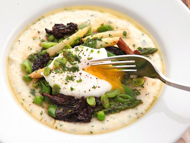 Closeup of cheesy grits with spring vegetables, topped with a poached egg that has been burst with a fork.