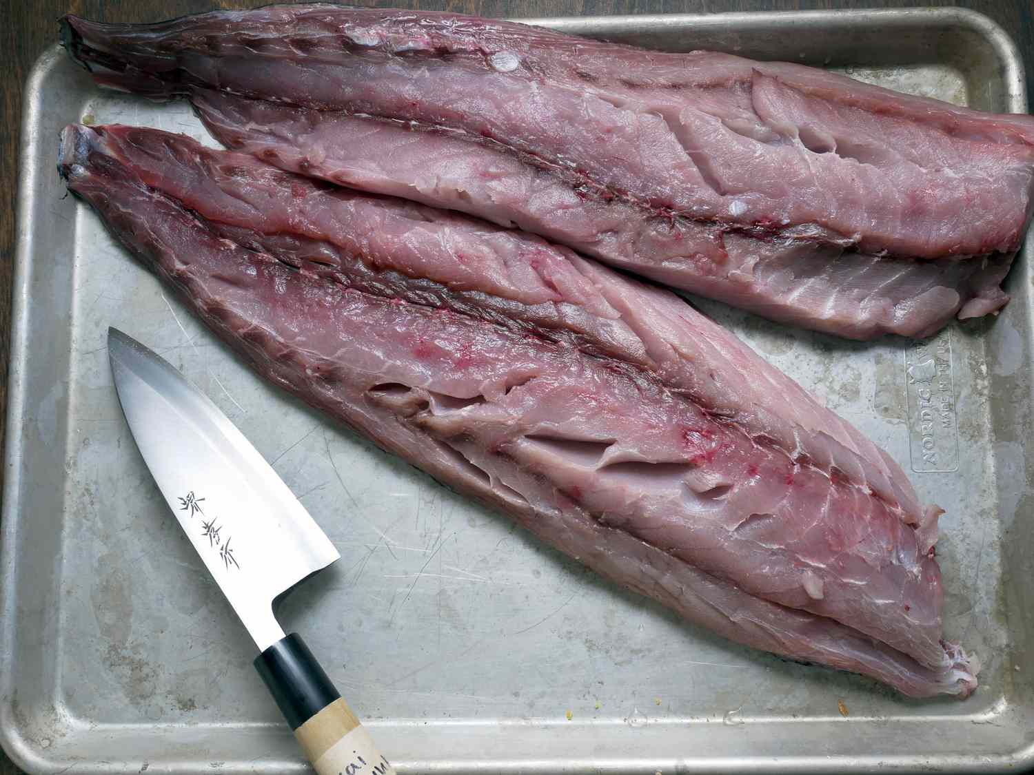 two bluefish fillets on a sheet pan with a deba knife