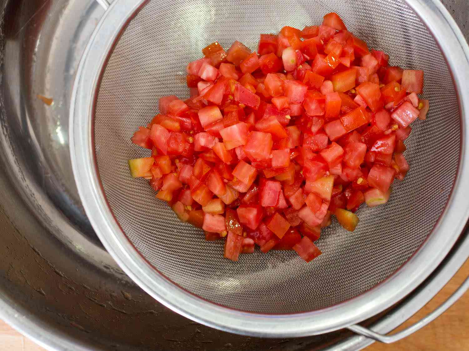 Draining salted diced tomatoes in a fine-meshed sieve to reduce the water that ends up in the final dish.