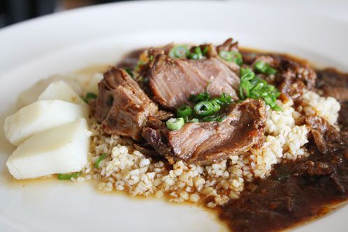 A plate of Sichuan braised pork cheeks served over rice and sprinkled with sliced green onion. Several chunks of daikon sit to one side and the braising liquid has started to pool around the rice.