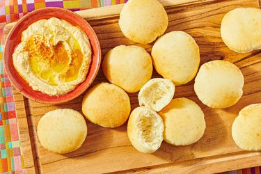 A wooden board with pita bread and a bowl of hummus