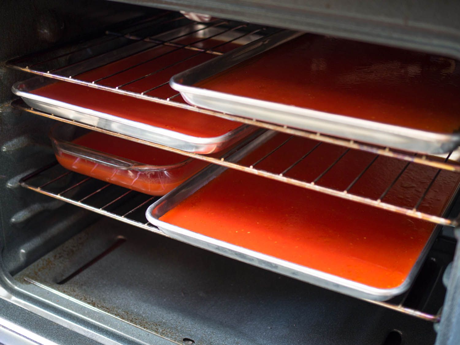 Several rimmed baking sheets and pans on racks in an oven filled with tomato water.