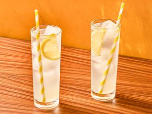 Two glasses of iced lemon drinks with striped straws on a wooden surface