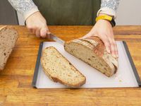 a person cutting a loaf of bread on the oxo large cutting board