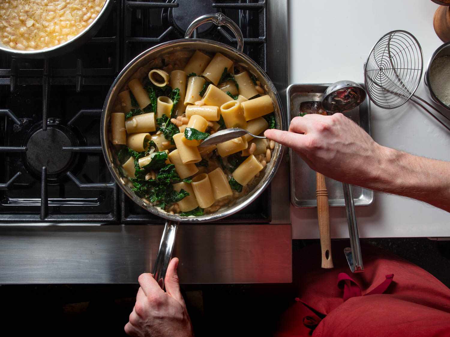 Overhead of stirring a skillet of pasta with beans and greens.