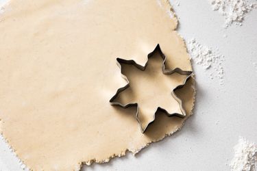 A starshaped cookie cutter on rolled dough sprinkled with flour on a surface