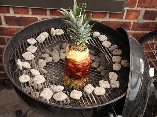 Formed marinated pork meat layered and skewered between top and bottom of whole pineapple vertically roasting on charcoal grill