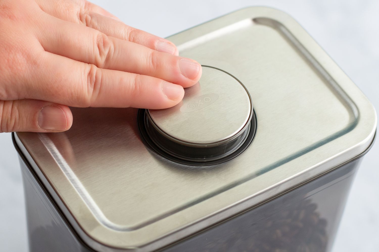 A hand pushing the top of the The OXO POP Coffee Container