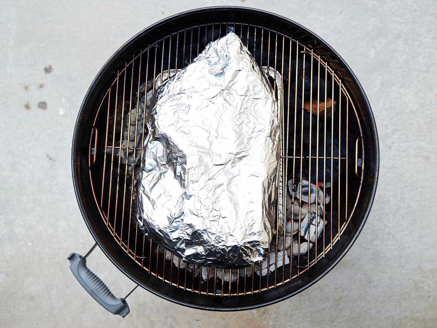Foil-wrapped brisket on a charcoal grill