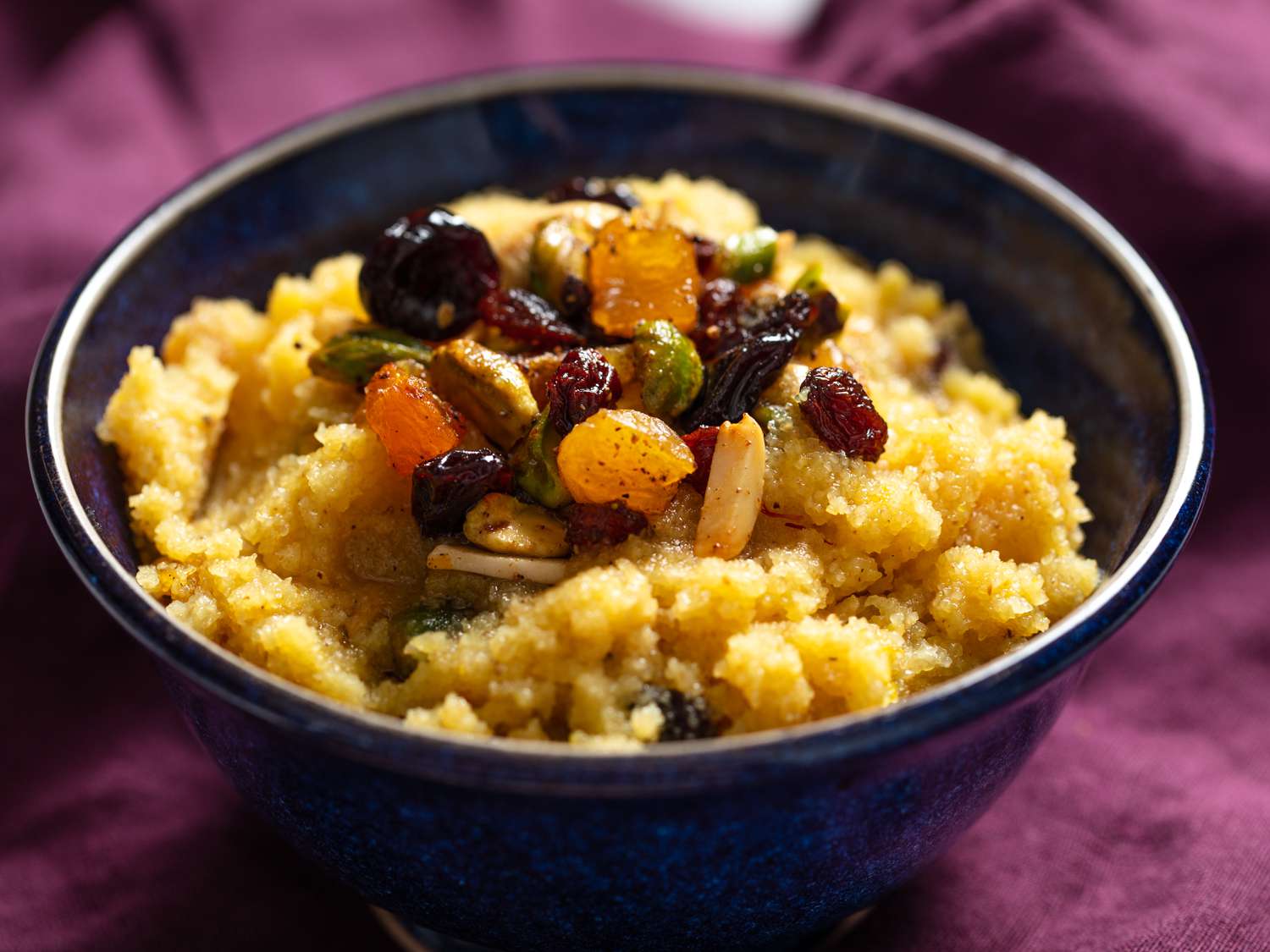 Bowl of semolina halva topped with spiced nuts and dried fruit