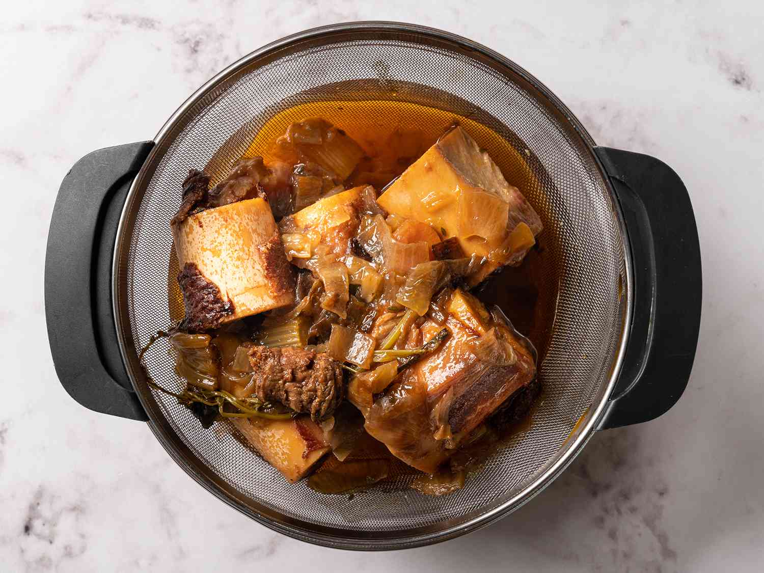 Beef stock being strained with a mesh strainer