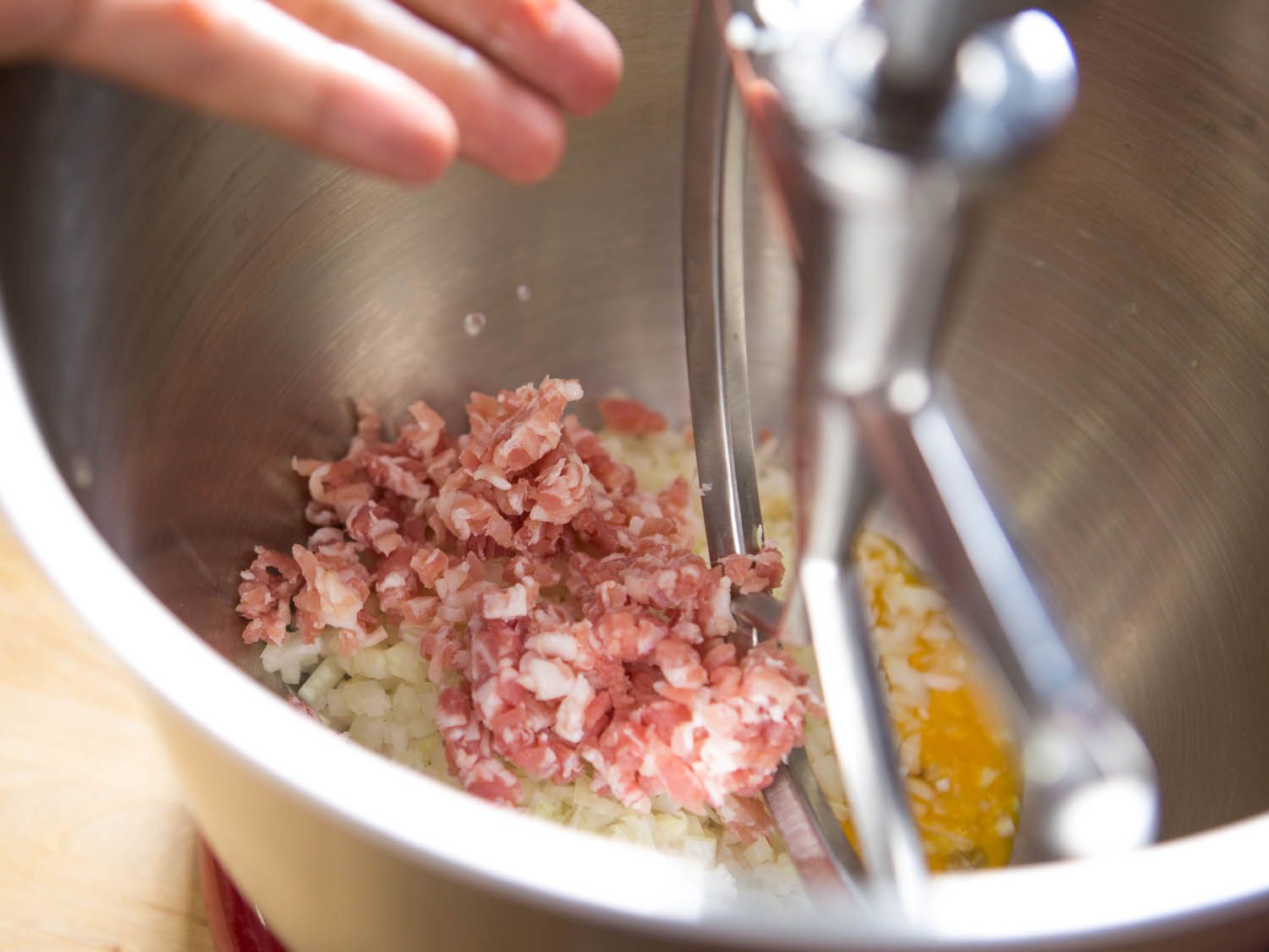 Minced pancetta in bowl of stand mixer with minced onion and egg.
