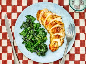 Sliced chicken breast on a plate with sautéed kale.